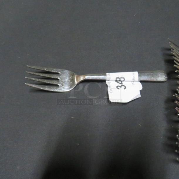 Lot of 15 serving forks on display, one fork centered. Metal finish, minimal wear, tag indicating item number 348 attached.