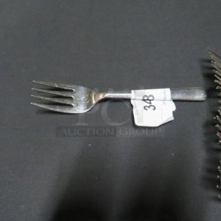 Lot of 15 serving forks on display, one fork centered. Metal finish, minimal wear, tag indicating item number 348 attached.