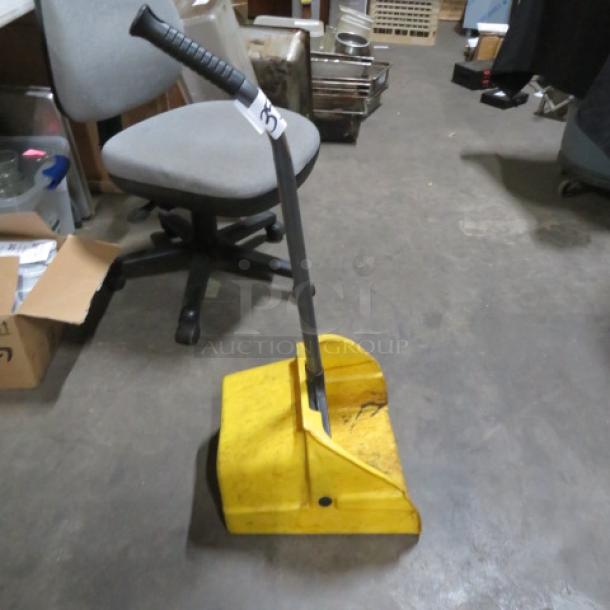 Yellow commercial dust pan with long black handle, moderate wear, visible scuff marks. Ideal for industrial cleaning tasks.