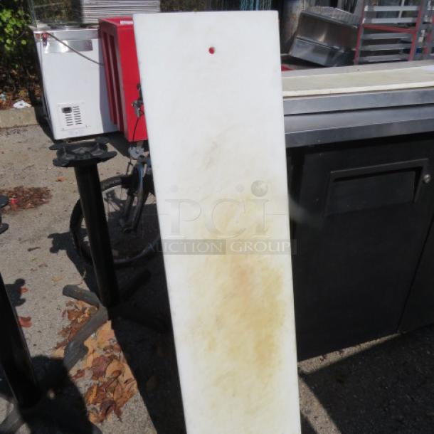 White plastic cutting board, 48x12 inches, with hanging hole. Shows signs of use with light staining. Suitable for kitchen use.