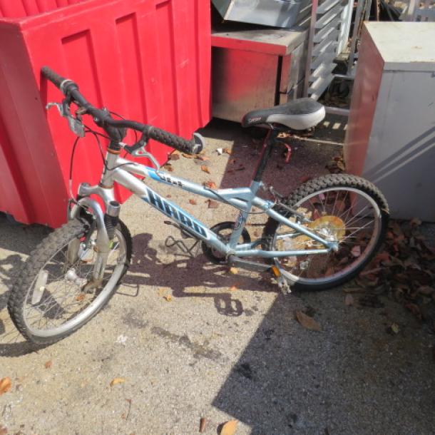 Harro blue child's bicycle with front suspension, black handlebars, and padded seat. Visible wear and outdoor storage signs.