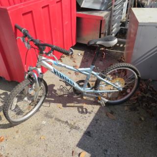 Harro blue child's bicycle with front suspension, black handlebars, and padded seat. Visible wear and outdoor storage signs.