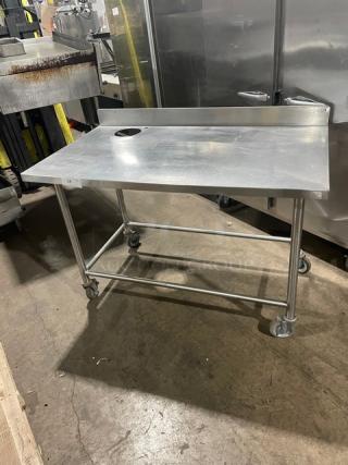 Commercial stainless steel worktop/prep table with back splash, round cut-out, and casters for mobility.