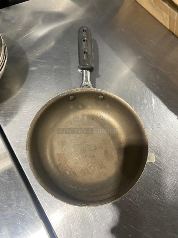 Commercial round fry pan with black grip handle, metal construction, slightly worn condition. No visible markings.