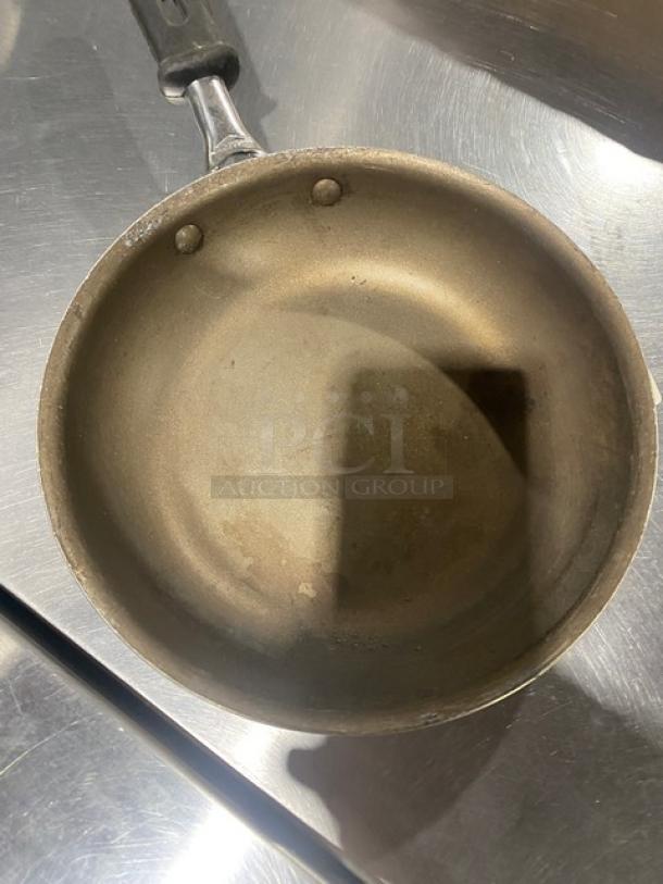 Commercial round fry pan with black grip handle, showing signs of use. Durable design, ideal for heavy-duty cooking.