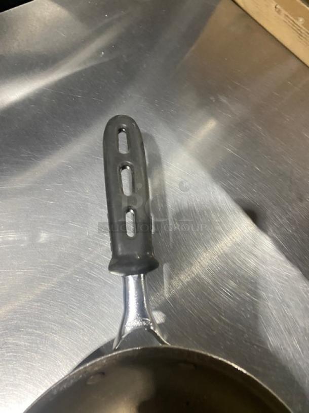 Commercial round fry pan with black grip handle, seen on a stainless steel surface. Features durable metal construction.