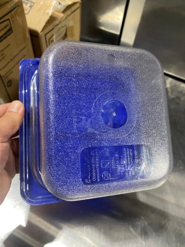 Carlisle clear polycarbonate food storage container with blue lid, shown in hand. Durable material, ideal for commercial use.