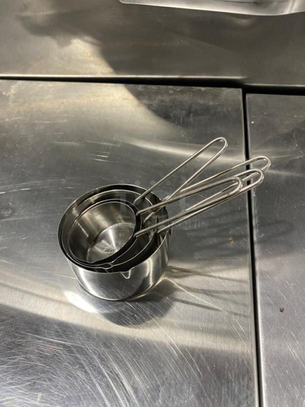 New commercial stainless steel measuring cup set, nested, with wire handles. Ideal for precise measurements.