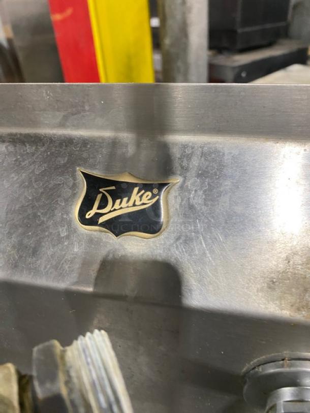 Duke Manufacturing stainless steel 3-compartment sink, featuring side drain boards, backsplash, and swing spout faucet. Logo shown.