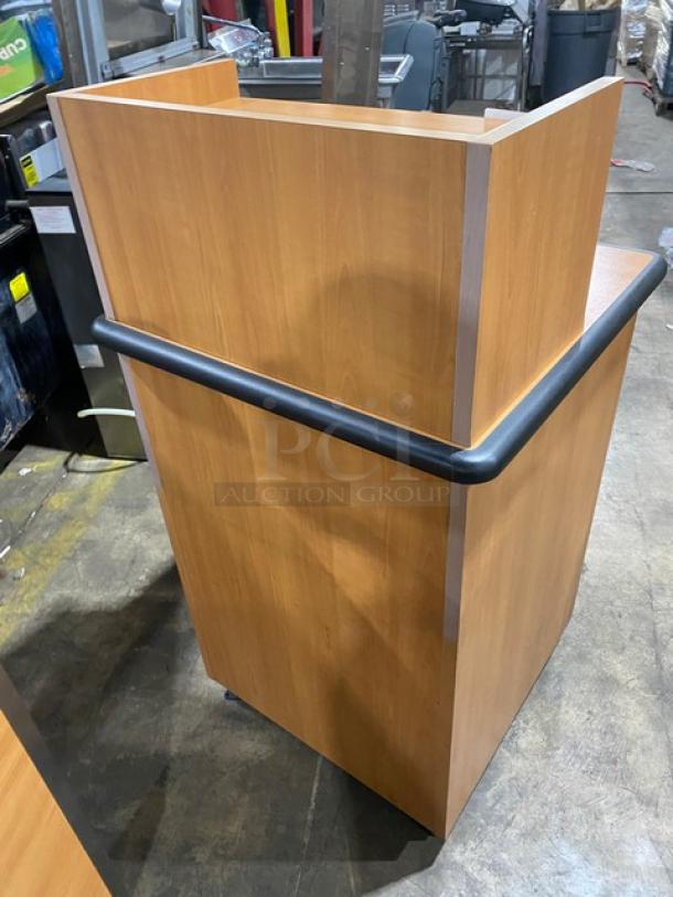 Commercial wooden enclosed recycle-style receptacle and trash cabinet with upper serving tray storage. Features black bumper and sits on legs. Appears in good condition.
