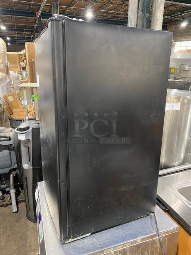Galanz GLR33MBKE23 black single-door mini refrigerator, 120V, commercial use, shows surface wear, free-standing design.
