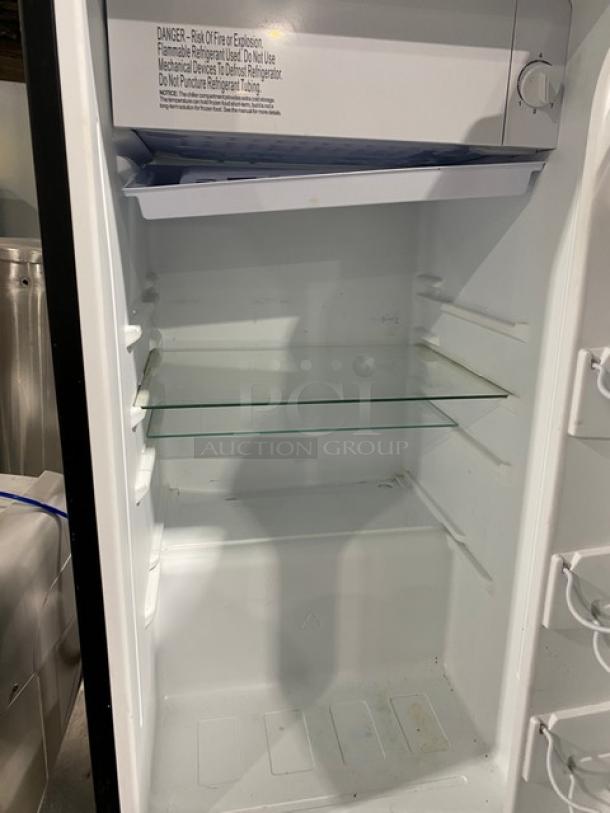 Galanz GLR33MBKE23 mini refrigerator open, single glass shelf, white interior, model and safety label inside.