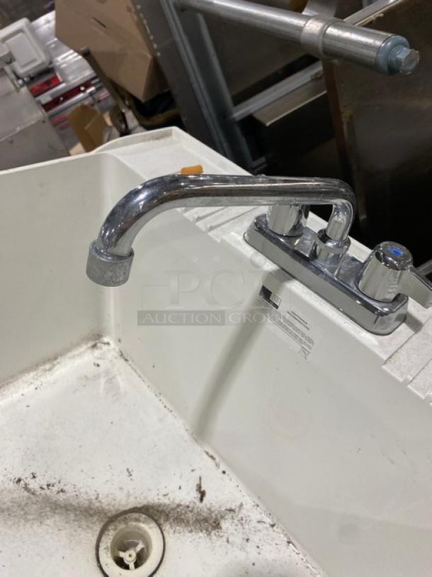 Commercial white single-compartment mop sink with swing spout faucet and legs, visible wear, ideal for utility use.