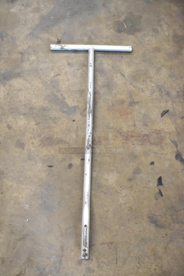 A worn, metal T-shaped tool on a concrete floor, showing signs of rust and wear.