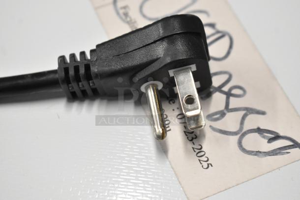 Close-up of a black power plug with visible prongs. A handwritten tag shows a date: 07-23-2025.