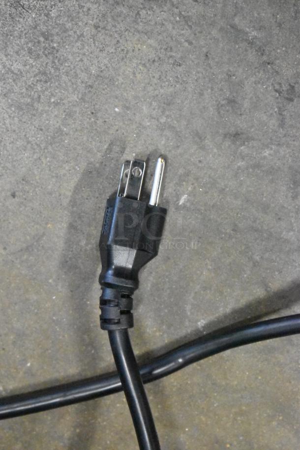 Close-up of black power cord plug on concrete floor, likely for the Avantco 178GDC40HCW merchandiser refrigerator.