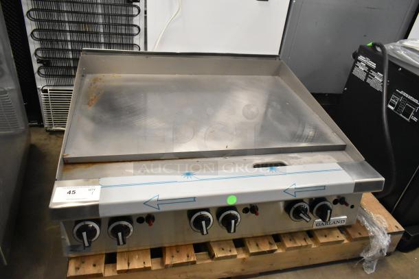 Brand new Garland stainless steel commercial flat top griddle, scratch and dent, on wooden pallet, with control knobs visible.