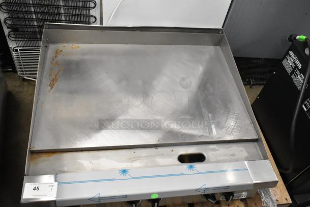 Brand new Garland stainless steel commercial flat top griddle with minor scratches and markings. Model tag visible.