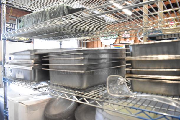 Auction lot featuring stainless steel drop-in bins, chafer lids, salad plates, and bowls on metal shelves. No shelving unit included.