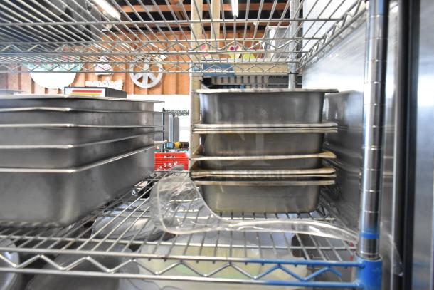 Stainless steel drop-in bins and chafer lids stacked on metal shelving. Includes salad plates and bowls. No shelving.