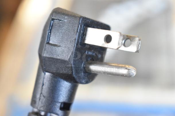 Close-up of a black electrical plug with three prongs, attached to a 2018 Continental CPA93 stainless steel commercial pizza prep table.