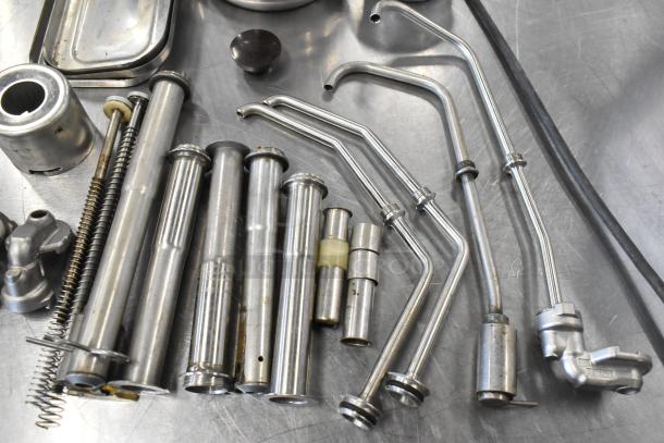 Lot of various metallic server pump parts, including pipes, springs, and connectors, in used condition on a metal surface.