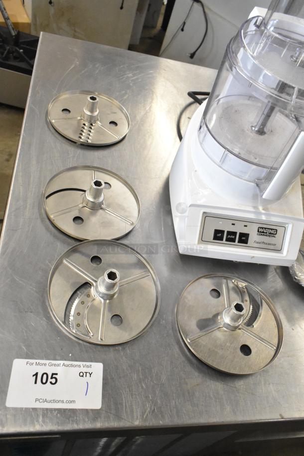 Waring food processor with 2 S blades, 6 slicing blades, 1 grating blade, 120 volts, 1 phase, on industrial surface.