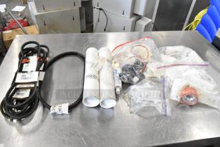 Lot of miscellaneous items including rubber belts, PVC tubes, and bagged parts on a metal table, various conditions.