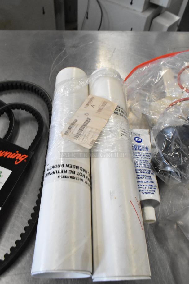 Lot of miscellaneous items including belts, tubes, and plastic components on a metal surface. Various labels visible.