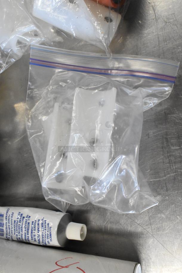 Lot of various items including white plastic pieces in bags and a tube with text labeled "silicone grease," on metal surface.