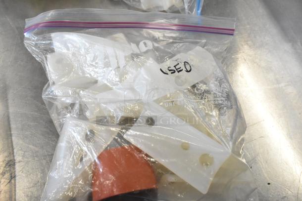 Lot of various items including belts and pieces in a clear zip bag marked "USED," placed on a metal surface.