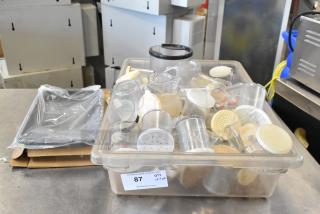 Lot of various items including poly seasoning shakers in a transparent bin. Shakers have white lids. Auction tag visible.
