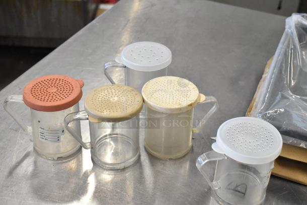 Lot of five clear poly seasoning shakers with varied lid colors, slight wear visible, on a stainless steel surface.