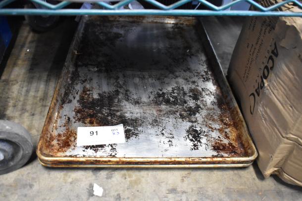Three metal baking pans with rust and wear, auction tag number 91 visible, indicating multi-bid lot.