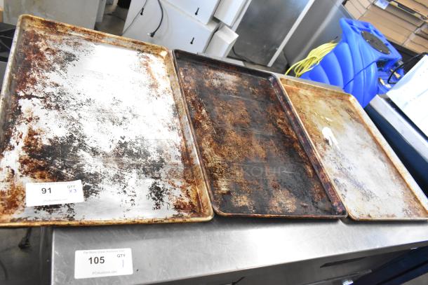 Three metal baking pans with signs of wear, featuring rust and discoloration. Labels indicate auction lot numbers 91 and 105.