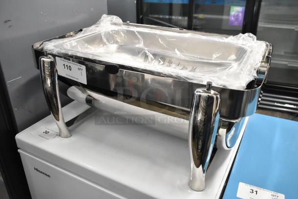Stainless steel chafing dish with rolling lid stuck, polished handles, and plastic wrap. Auction tag visible: Item 110.
