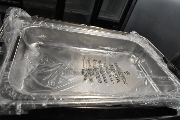 Metal chafing dish with rolling lid, lid is stuck. Wrapped in plastic, includes warning label. Ideal for catering use.