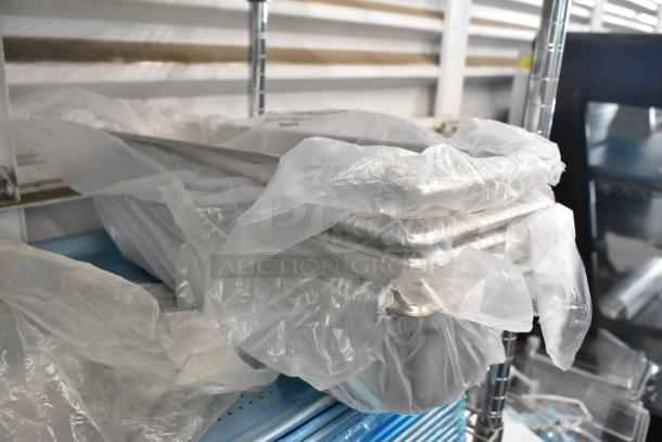 Brand new metal baking pans wrapped in plastic, part of a lot including stainless steel drop-in bins; pristine condition.