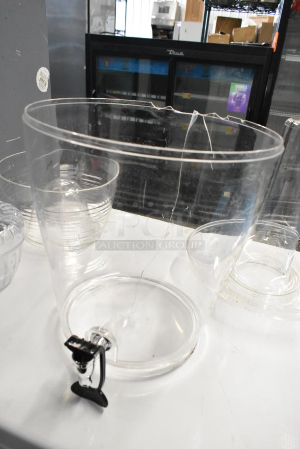 Two clear poly beverage dispensers with visible cracks, labeled "scratch and dent." New condition, features a spigot.