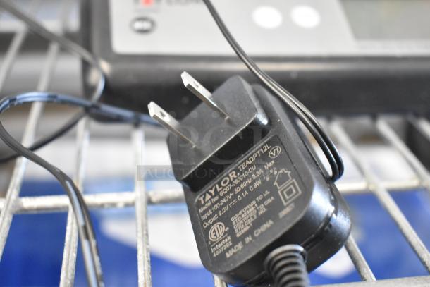 Taylor TE22OS digital scale charger, model TEADPT-12L, with specifications, shown on a metal surface.