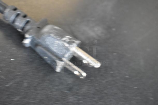 Close-up of a power plug for a Nemco 6055A food warmer, showing prongs and part of the cable, on a dark surface.