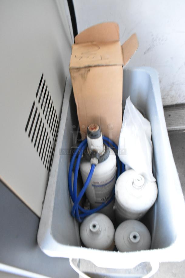 Blurred image of equipment items in a container, possibly related to the Alpine OP238EC ice cream machine.