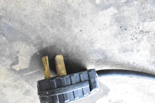 Close-up of a two-prong power plug attached to a cable, lying on a textured floor surface.