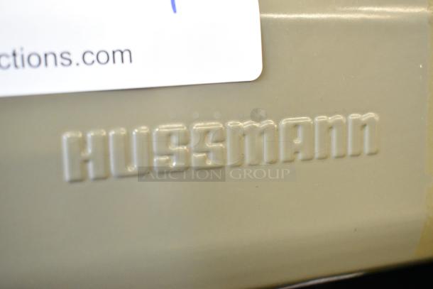 "Embossed Hussmann logo on GSVM-4060 commercial merchandiser. Beige metal surface, part of grab n go reach in unit."
