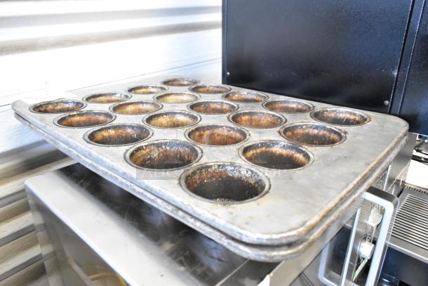 Two metal 20-cup muffin baking pans, showing signs of use, surface marks visible, suitable for large batch baking.