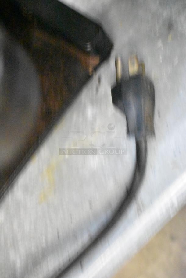 Blurry image of a power cord and metal surface, possibly part of a commercial espresso bean grinder.