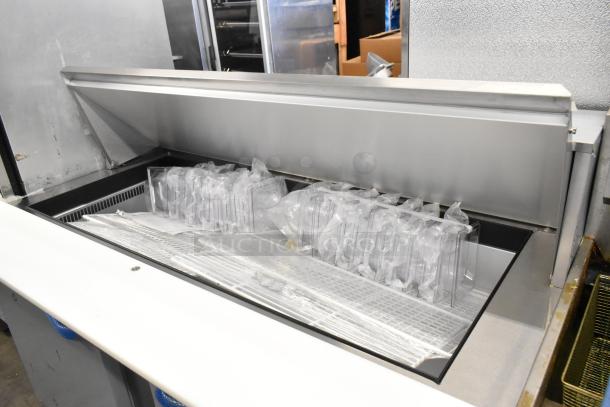 Brand new Traulsen UPT6024-LR stainless steel sandwich prep table, showing interior with sealed containers, on commercial casters.