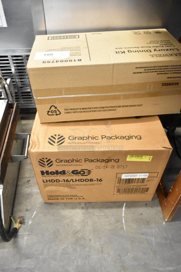 Two boxes labeled LHDD-16/LHDDB-16 by Graphic Packaging and Luxury Dining Kit plasticware set, shown in a warehouse setting.