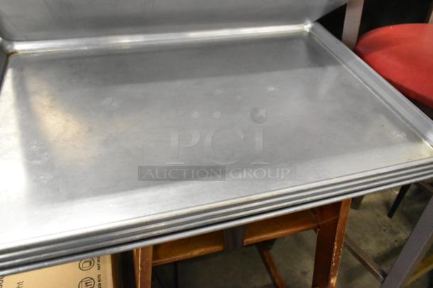 Seven metal full-size baking pans, stackable condition, ideal for commercial use; polished and sturdy material.
