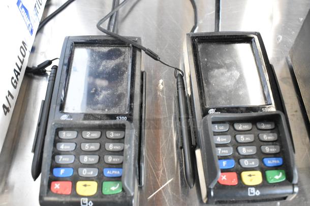 Two PAX S300 credit card readers with signs of wear; touchscreens show smudges. Keypads intact. Includes stylus attachments.